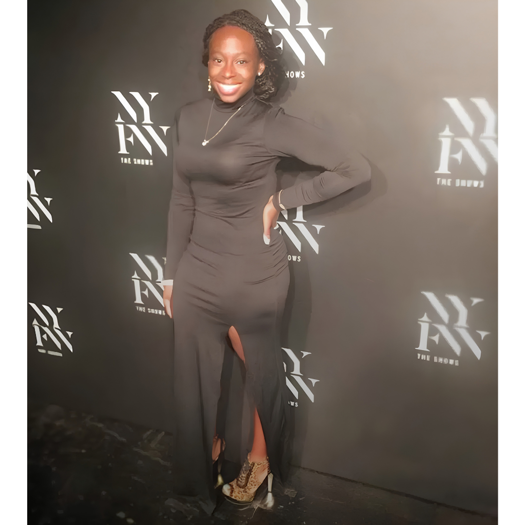 Ta'Quaryan in a black dress in front of the NYFW The Shows step-and-repeat backdrop at New York Fashion Week